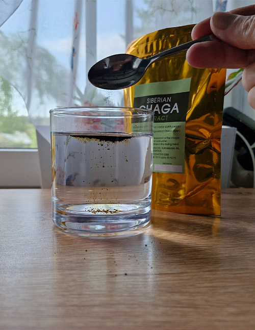 Correct method of preparing Chaga extract drink by sprinkling the powder over a glass of water without immersing the spoon.