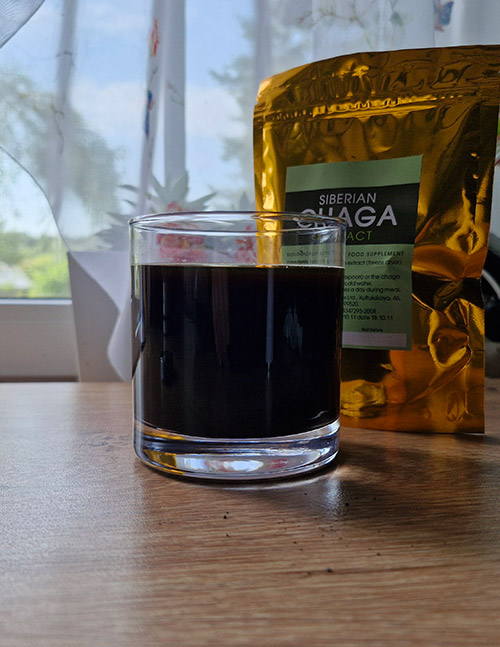 A glass of freshly prepared Chaga extract drink with rich dark color, standing next to a pack of Siberian Chaga extract.